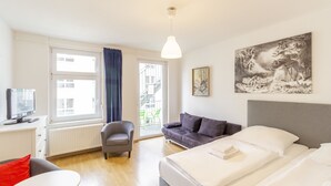 Une chambre d’hôtel avec un lit, un canapé, un bureau avec un ordinateur et une fenêtre avec des rideaux.