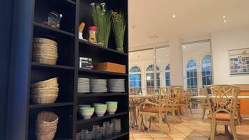 Ein Zimmer mit einer schwarzen Regaleinheit, die Körbe, Teller und Gläser enthält. Es gibt Korbstühle und einen Tisch mit einem Blumenstrauß.