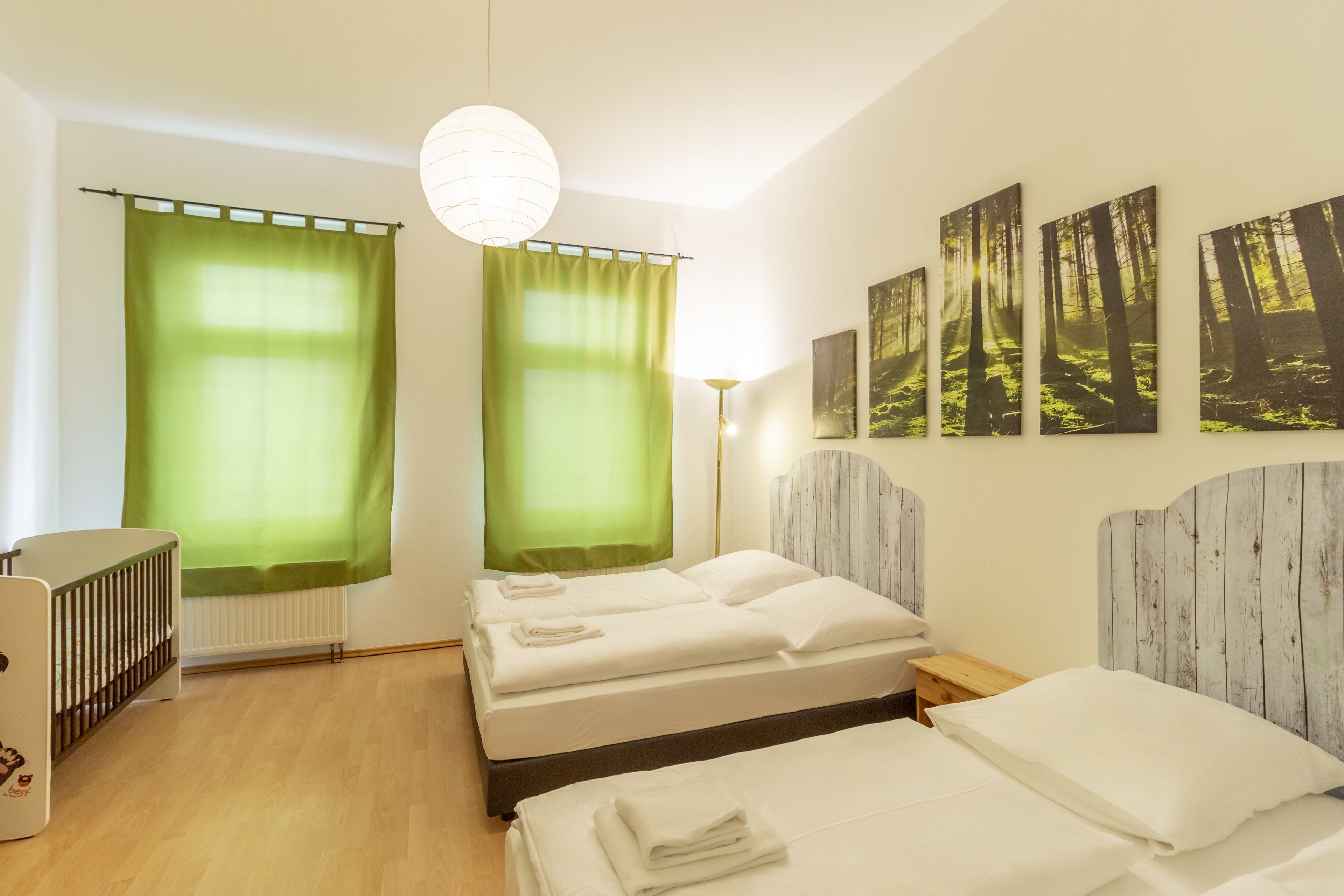 A hotel room with two beds, a crib, a radiator, and forest-themed wall art.