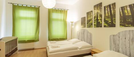 A hotel room with two beds, a crib, a radiator, and forest-themed wall art.