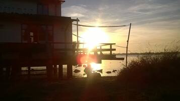 A pier with a view of the sunset over water, featuring a building with a balcony.