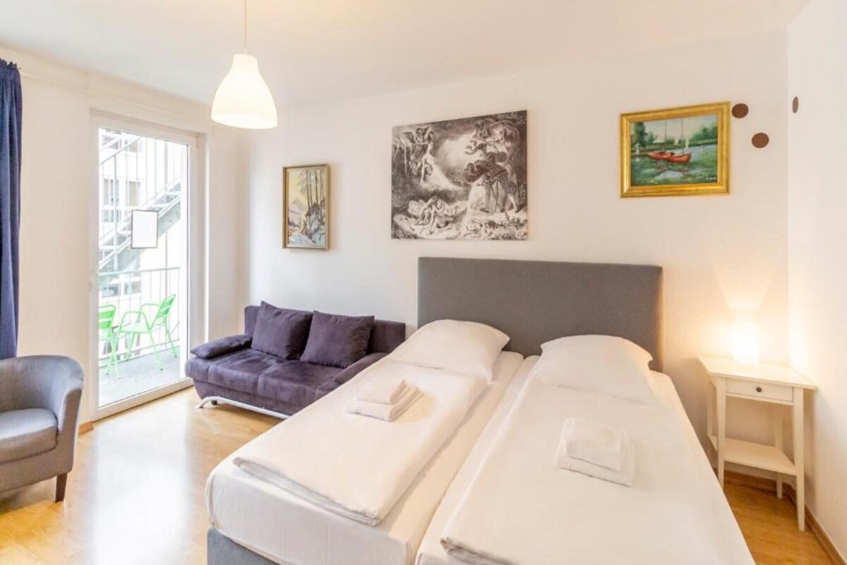 Habitación de hotel con dos camas, un sofá, una silla y obras de arte en las paredes.