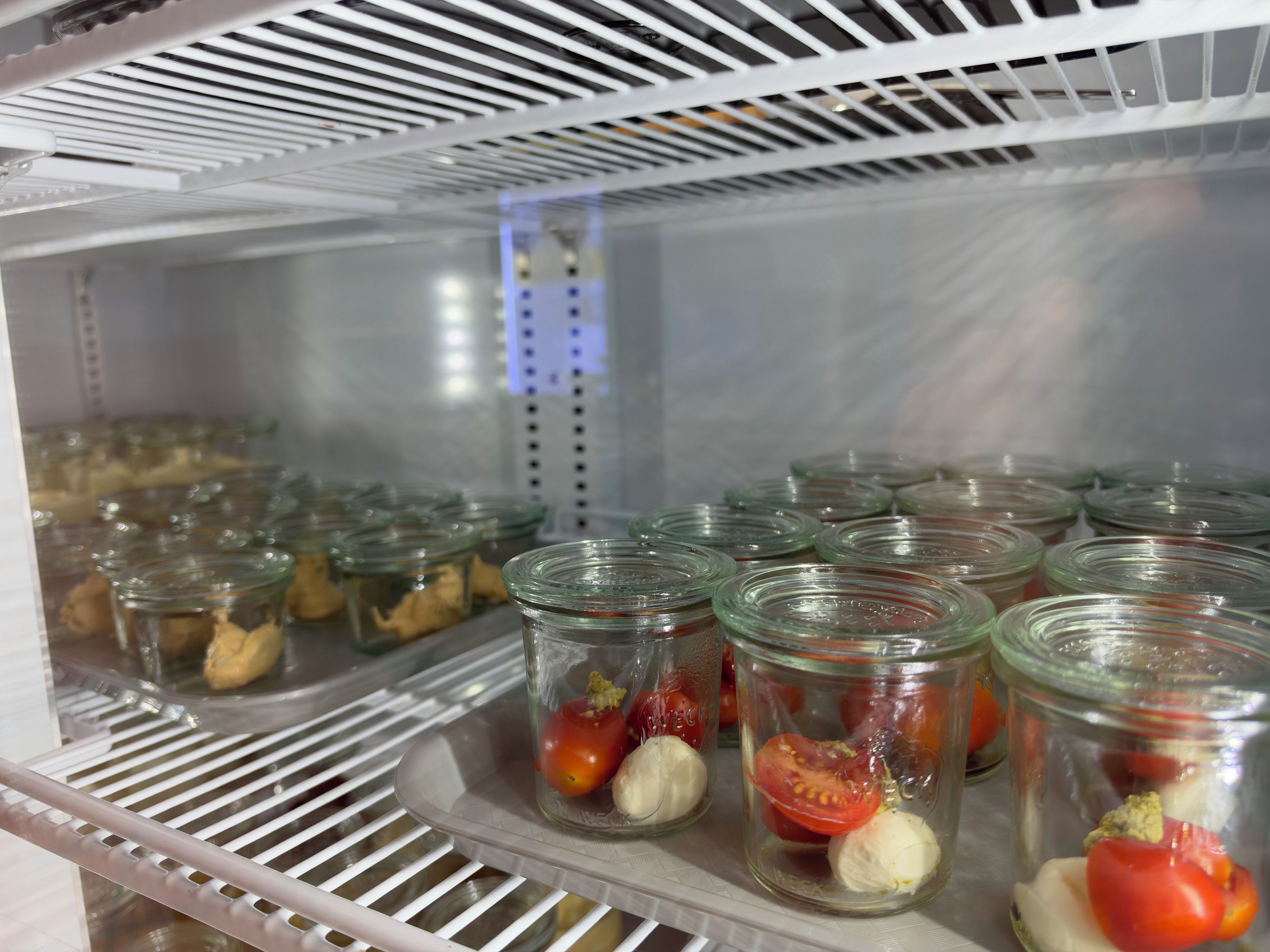Un espace de stockage réfrigéré, doté d’étagères où sont rangés des bocaux en verre contenant des aliments.