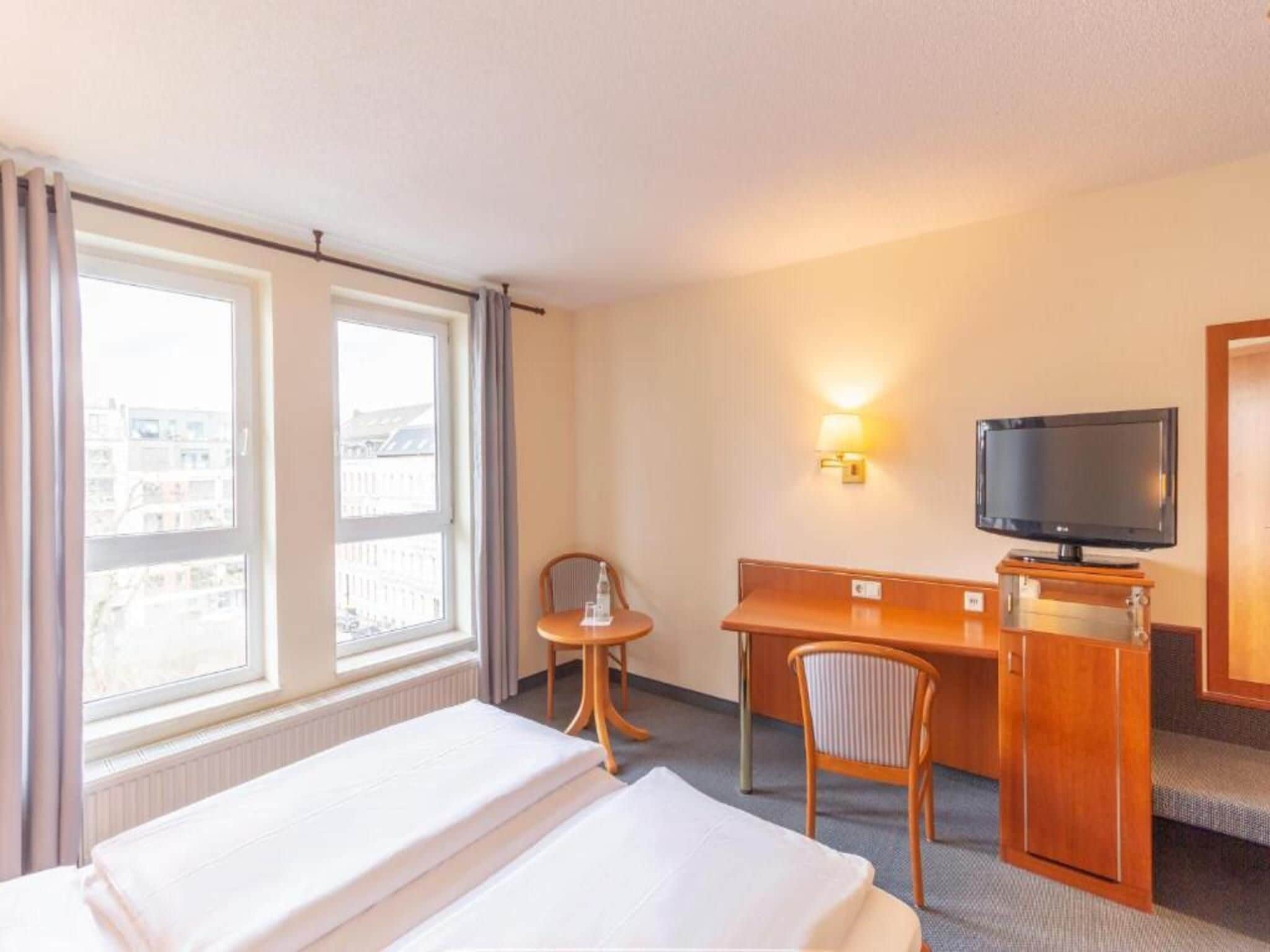 A hotel room with a bed, a desk, a chair, a television, and a window with curtains.