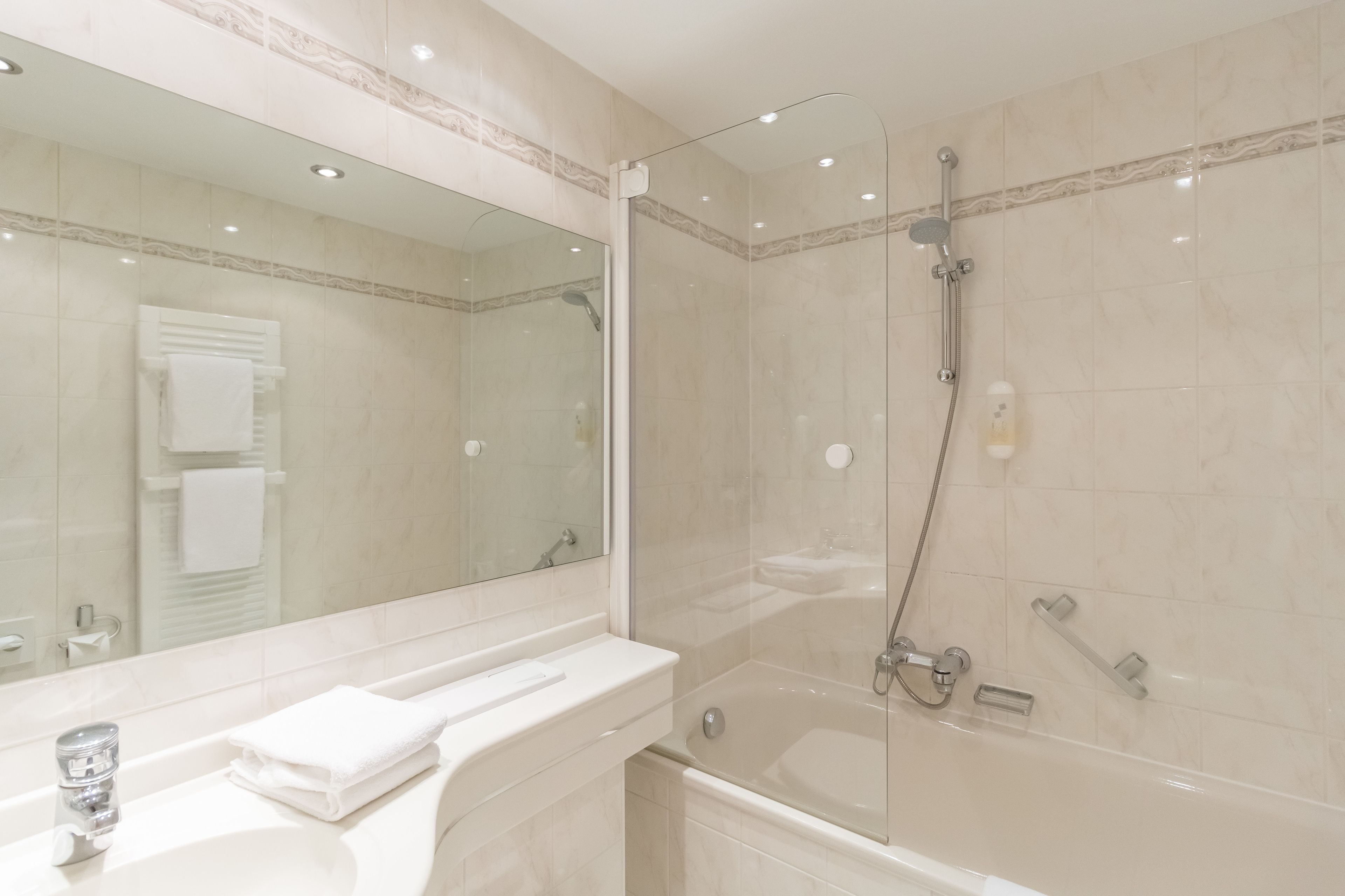 Un baño moderno con ducha de vidrio, un espejo grande y un lavabo blanco con una toalla.