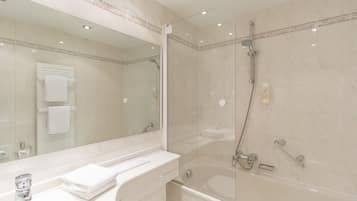 Un baño moderno con ducha de vidrio, un espejo grande y un lavabo blanco con una toalla.