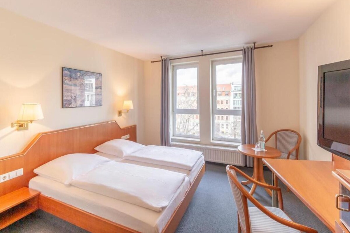 Habitación de hotel con dos camas, un escritorio, una silla, un televisor y una ventana con cortinas.
