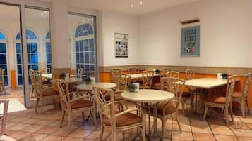 Un comedor con sillas de mimbre y mesas redondas, ventanas amplias y un cartel en la pared.