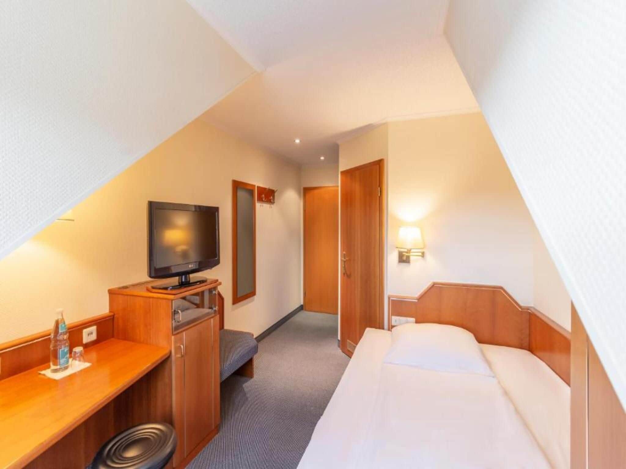 A hotel room with a bed, a desk with a television, a mirror, and a door.