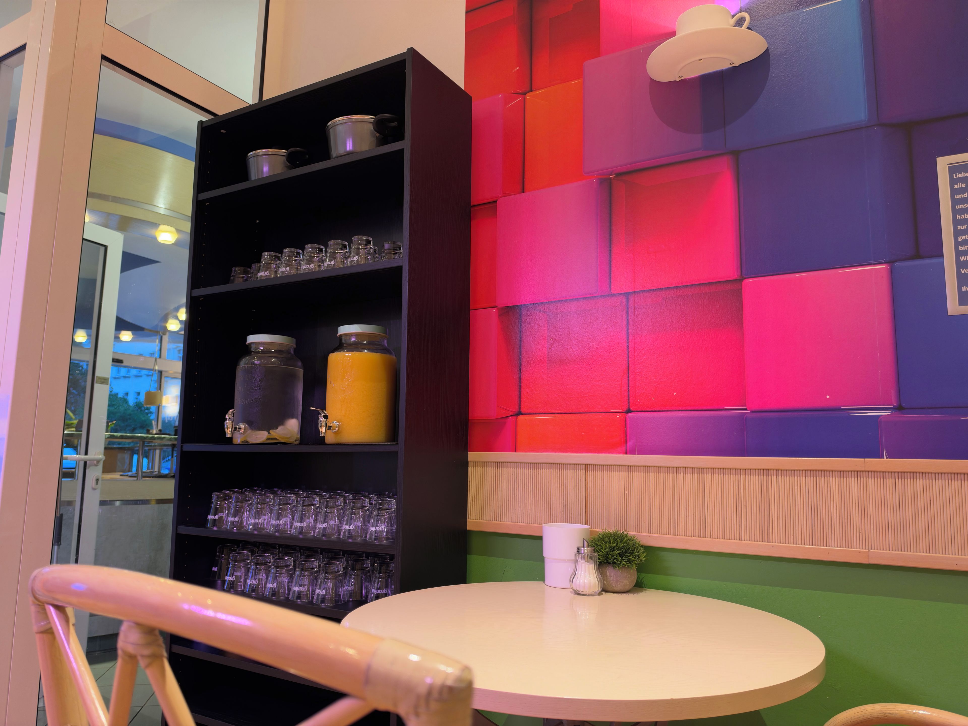 Una habitación con una mesa redonda, un estante con frascos, y una pared colorida.