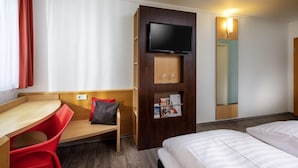 Une chambre d’hôtel comprenant un lit, un bureau avec une chaise, un téléviseur fixé sur un panneau en bois et un miroir au mur.