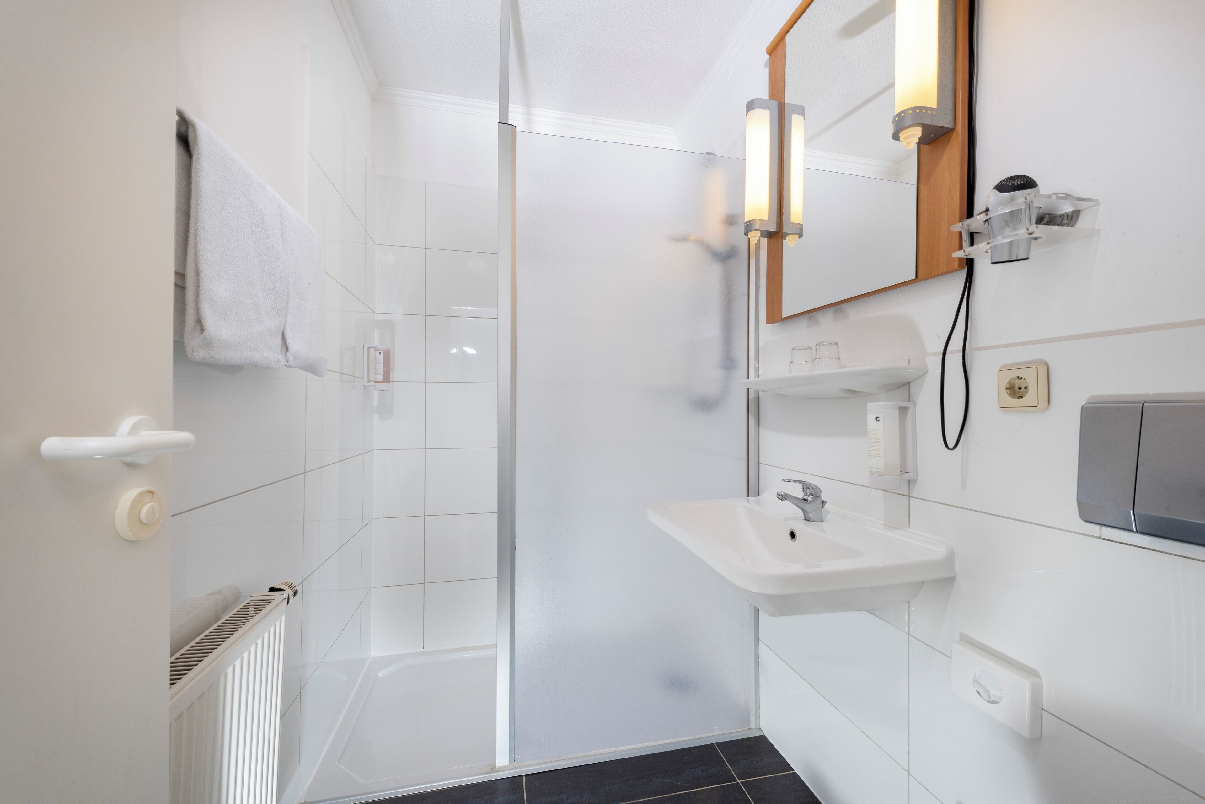 Une salle de bain moderne dotée d’une douche à parois de verre, d’un lavabo blanc et d’un miroir avec éclairage intégré.