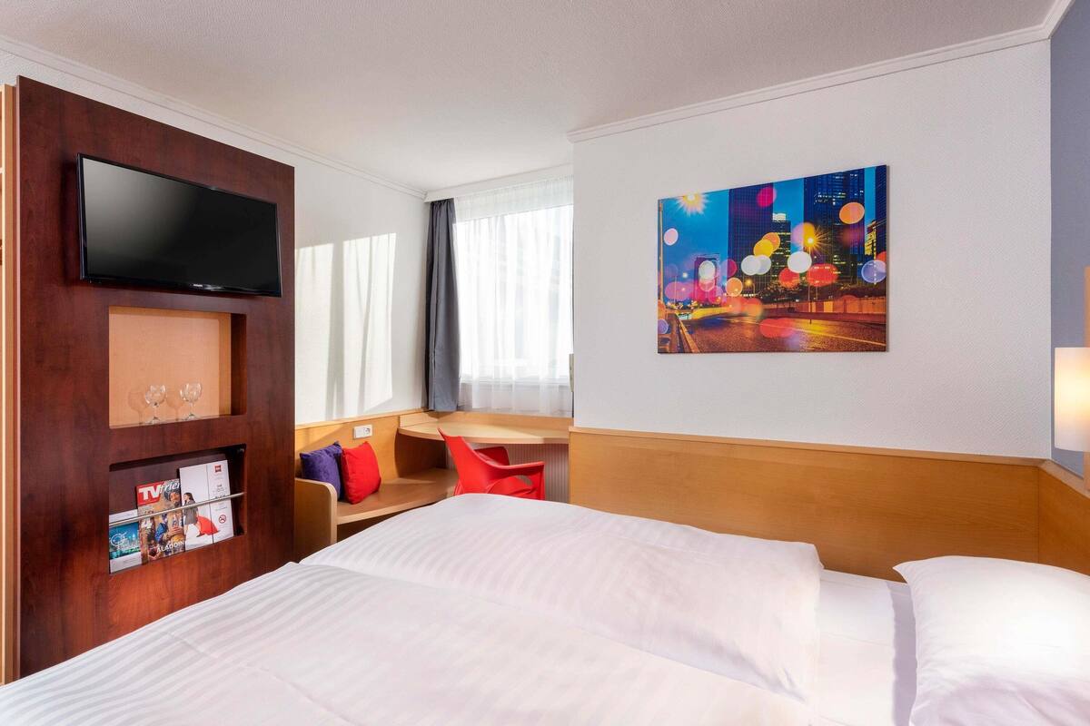 A hotel room with a bed, a TV, a painting, and a seating area with a table and chairs.