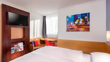 Habitación de hotel con cama, televisión, un cuadro y zona de estar con mesa y sillas.