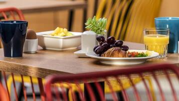 A breakfast table with a croissant, grapes, a glass of orange juice, a blue mug, and a white cup.