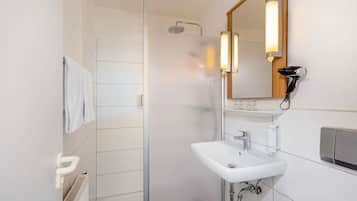 Un baño moderno con cabina de ducha de vidrio, un lavabo blanco e iluminación integrada en un espejo.