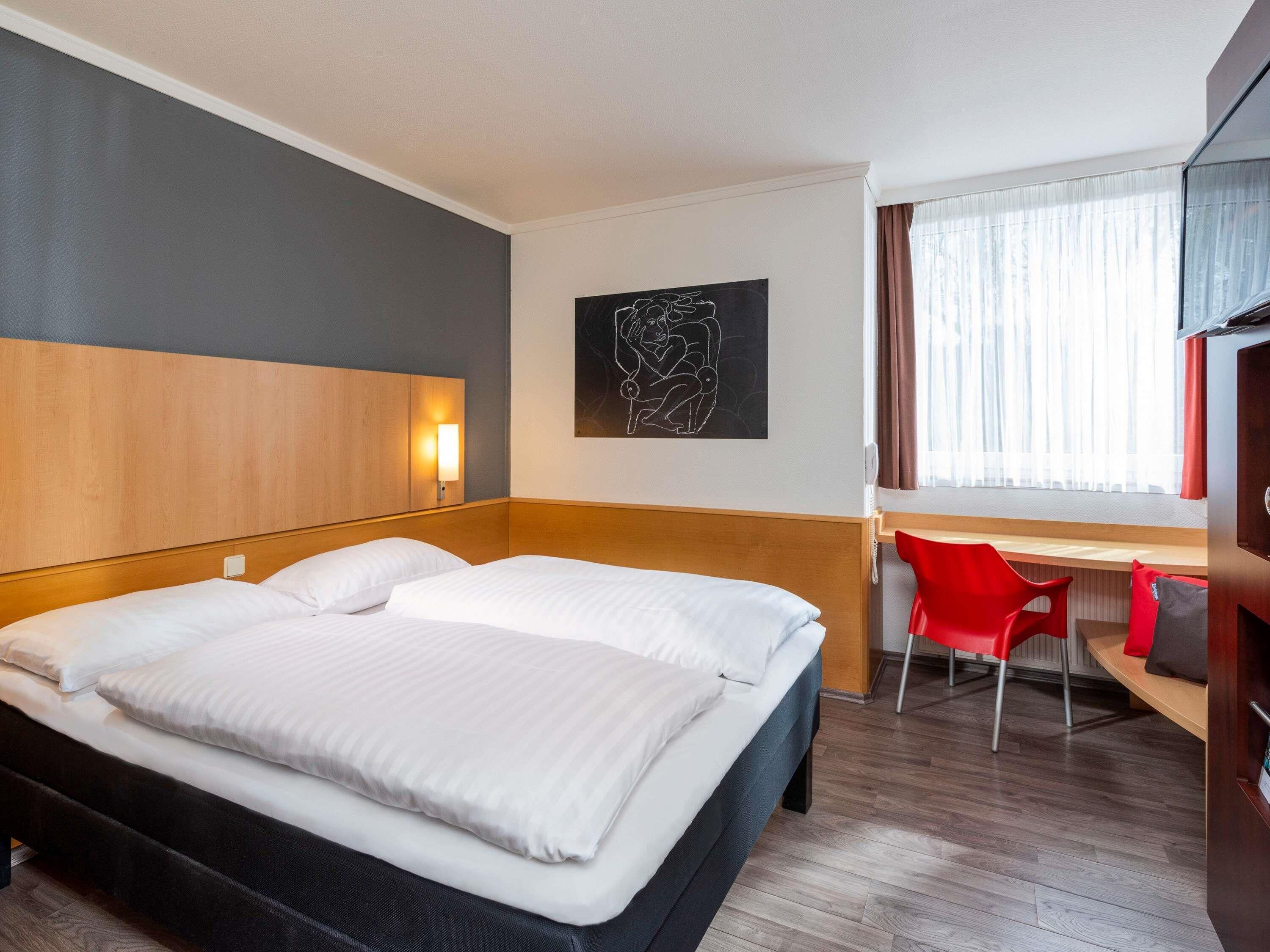 Hotellihuone, jossa on suuri sänky, työpöytä, tuoli ja ikkuna, jossa on verhot.