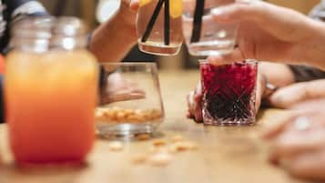 A group of people holding glasses with straws, one glass contains a red drink, and there are nuts on the table.