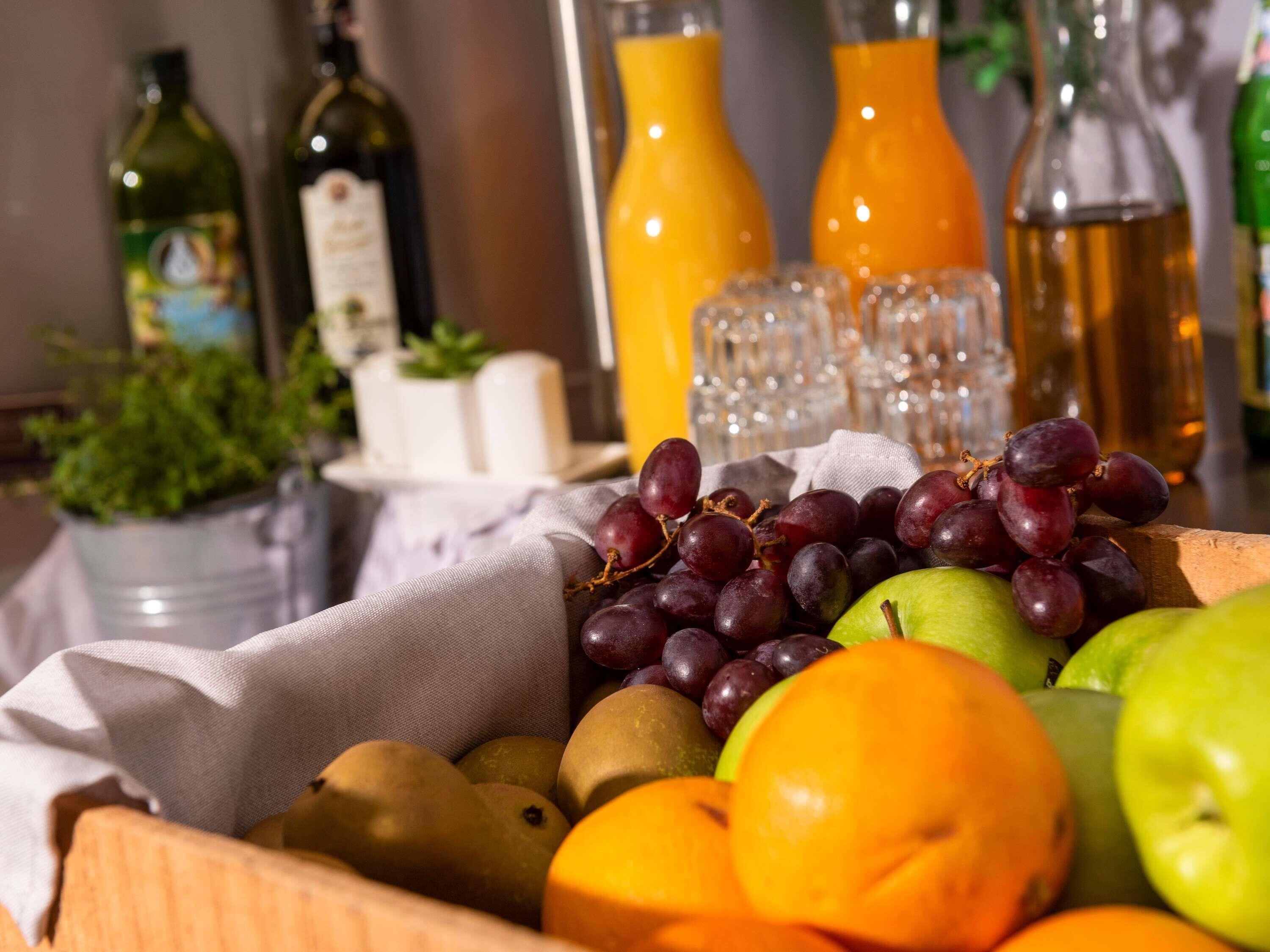 Ein Obstkorb mit Trauben, Äpfeln und Birnen, umgeben von Olivenölflaschen und Orangensaft.