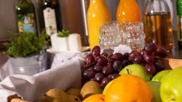 Una cesta de frutas con uvas, manzanas y peras, rodeada de botellas de aceite de oliva y jugo de naranja.