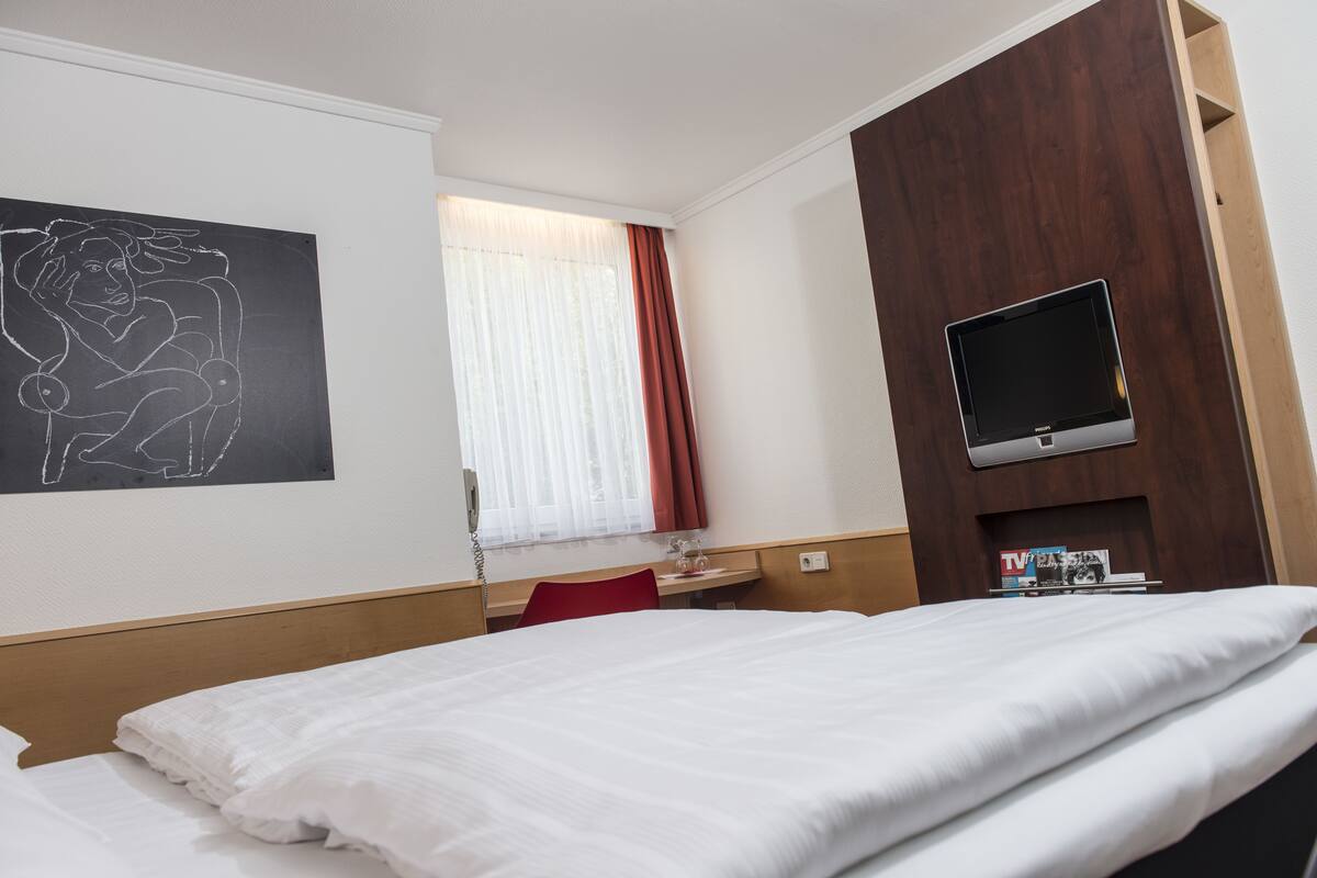 A hotel room with a bed, a desk, a TV, and a window with curtains.