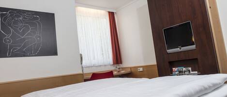 A hotel room with a bed, a desk, a TV, and a window with curtains.