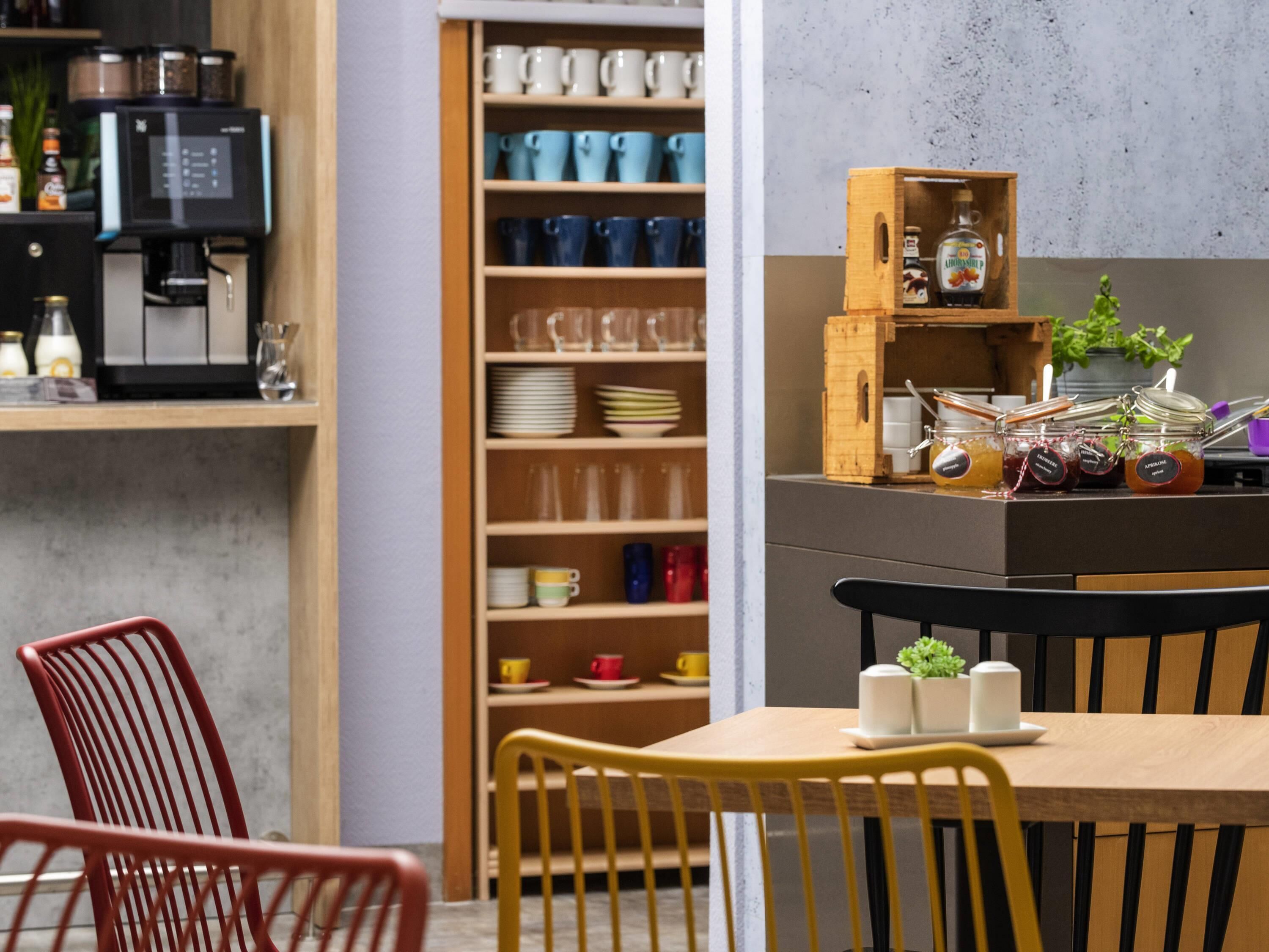 Una cocina moderna con cafetera, estantes con vajilla y un armario de madera con frascos.