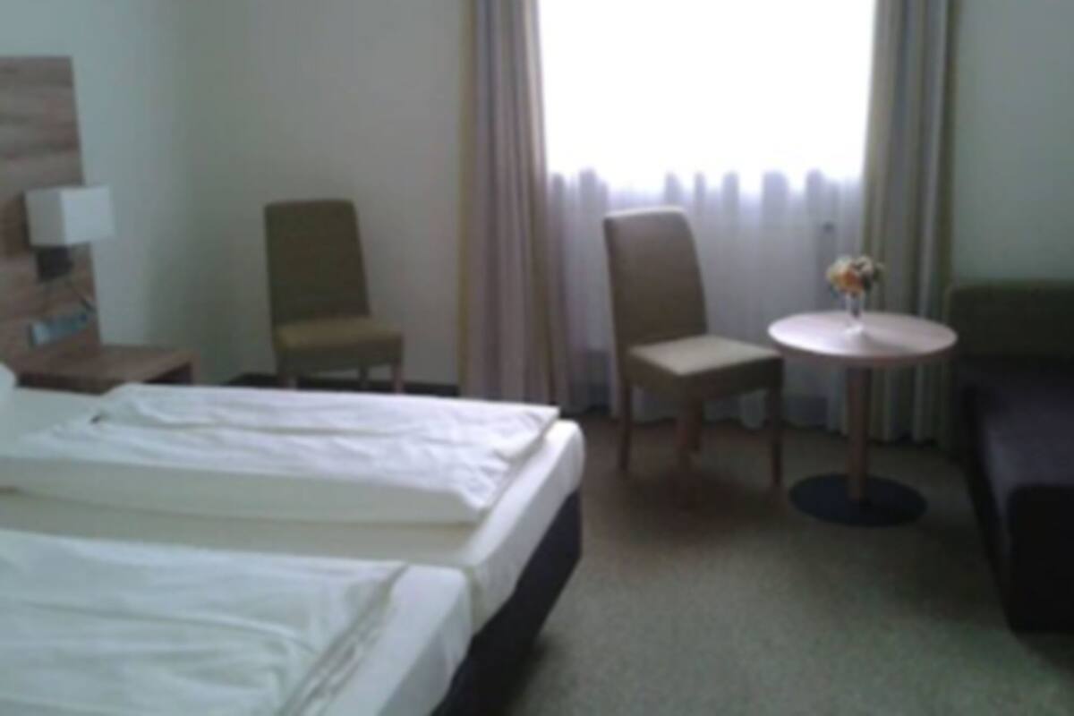Una habitación de hotel con dos camas, una mesita con un florero, dos sillones y un sofá.
