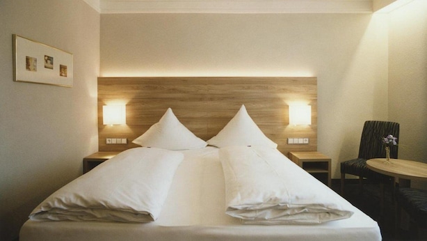 A hotel room with a large bed, two bedside tables, a chair, and a small table. - Hotel Jedermann (Munich)