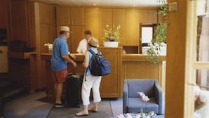 A reception area with wooden cabinets, a reception desk, and a seating area with a chair and a small table. - Hotel Jedermann (Munich)