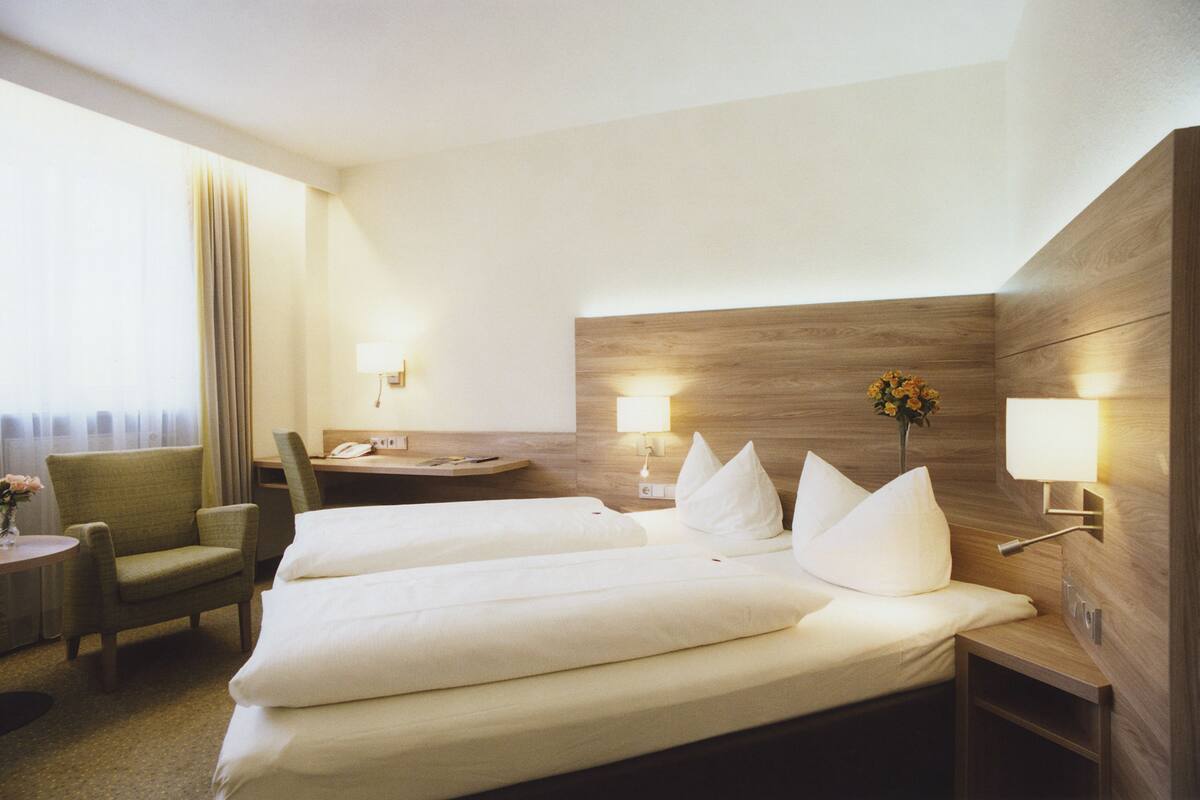 Habitación de hotel con dos camas, un escritorio, una silla y una pequeña mesa con un jarrón de flores.