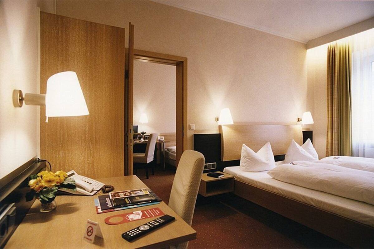 Habitación de hotel con cama, mesitas de noche, escritorio con lámpara, silla y televisión.