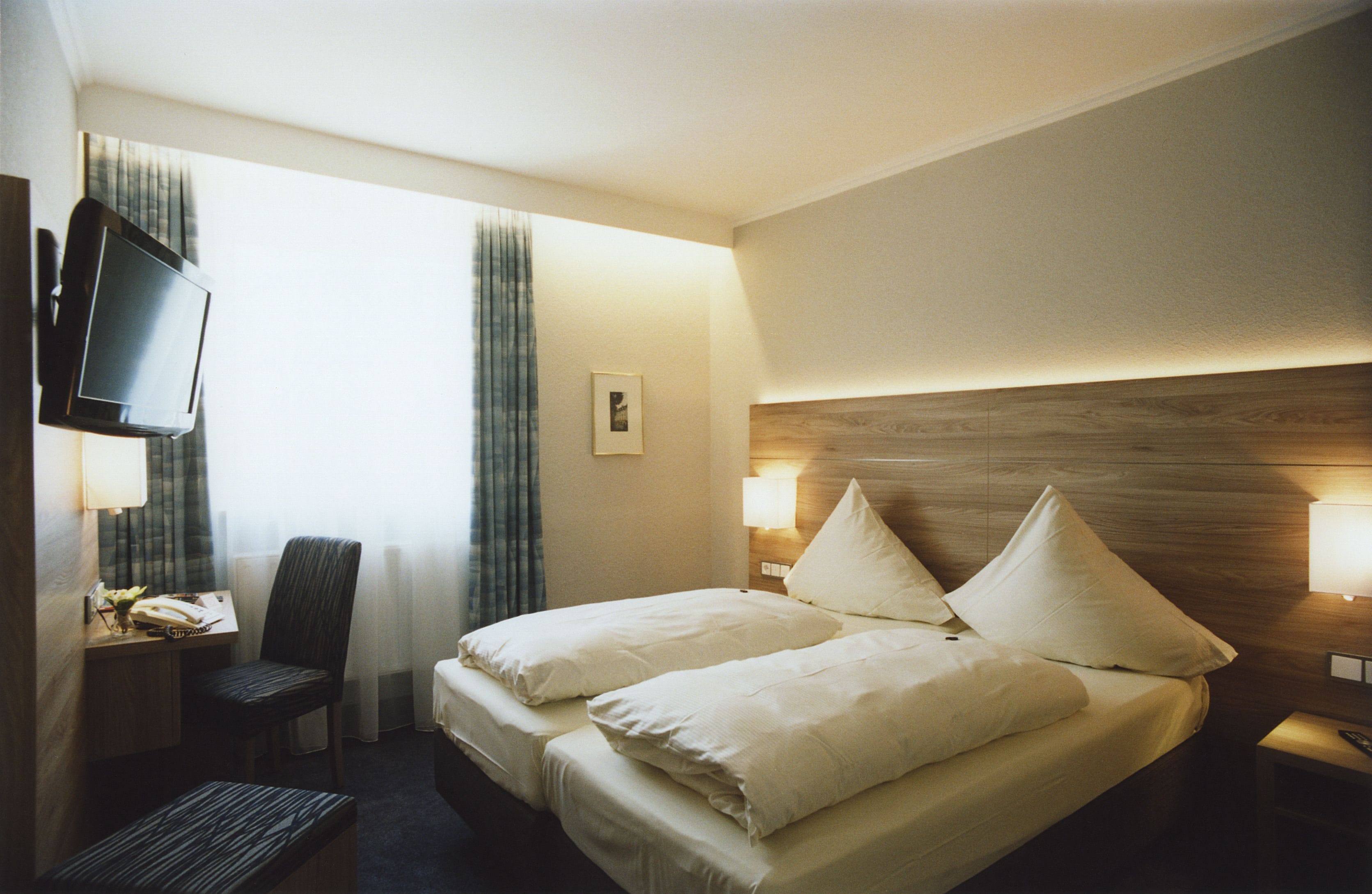 Een hotelkamer met een bed, een bureau, een stoel, een televisie en een nachtkastje met een lamp.