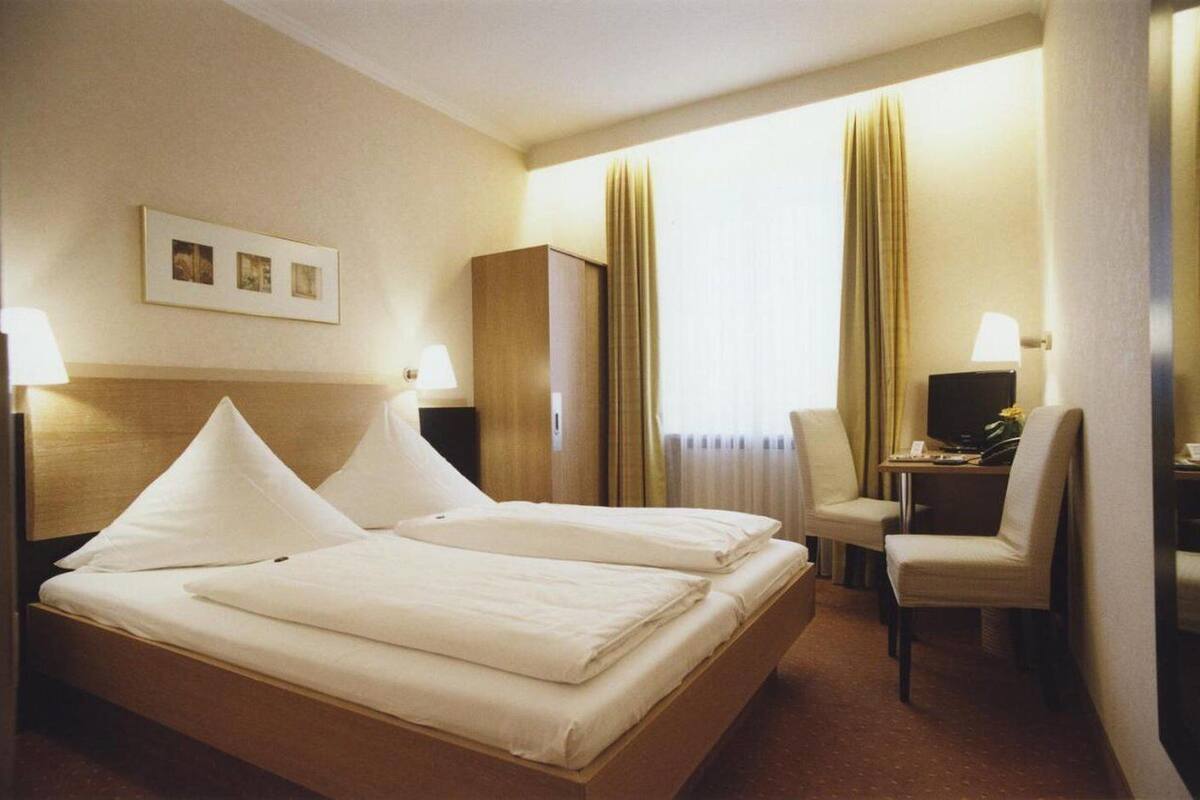 Una habitación de hotel con cama doble, escritorio con silla, televisor y armario.