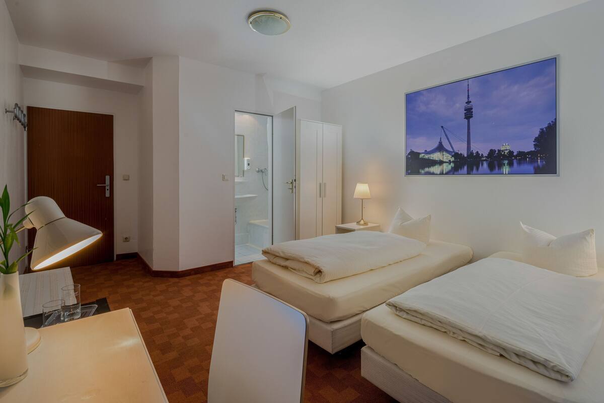 A hotel room with a bed, bedside table, lamp, and a painting of a cityscape.