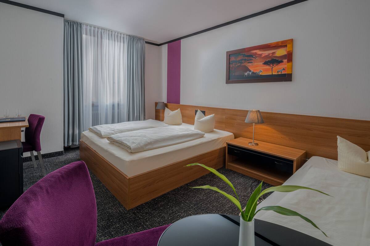 A hotel room with a bed, a desk, a chair, a nightstand, a lamp, and a painting on the wall.