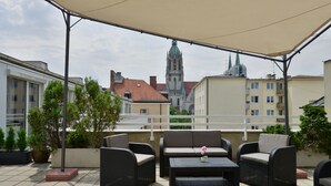Eine Terrasse mit Korbmöbeln, einem Blumentopf und Blick auf einen Kirchturm.
