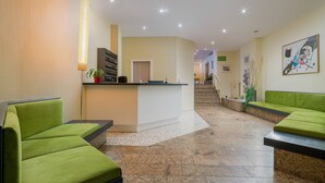 Eine Lobby mit grünen Sitzgelegenheiten, einem Empfangsbereich und einer Treppe zu einer anderen Etage.