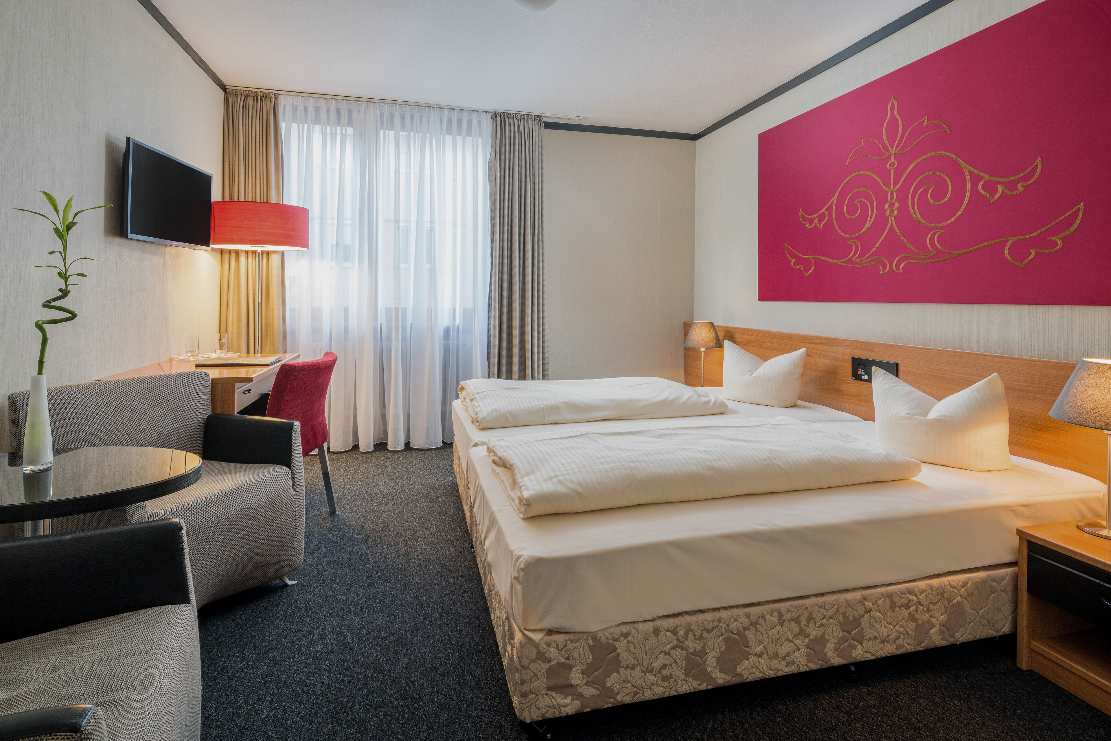 A hotel room with a bed, a desk, a chair, a TV, and a decorative wall piece.