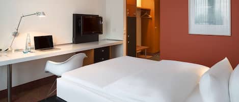 Una habitación de hotel con una cama, un escritorio con una computadora portátil, un televisor y un vestidor.