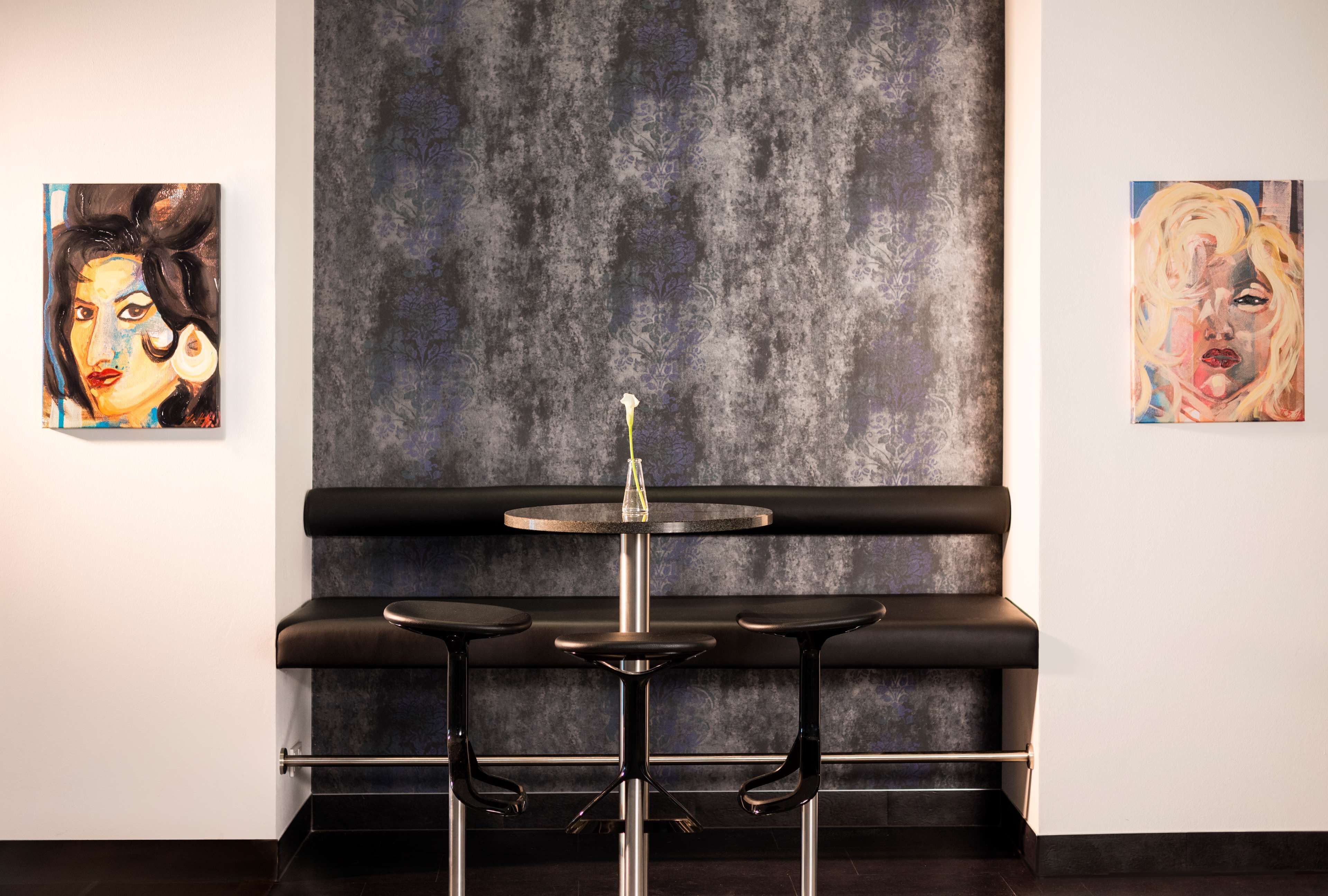 Un espace bar au design moderne, avec un comptoir et des tabourets noirs, et deux œuvres d’art accrochées aux murs.