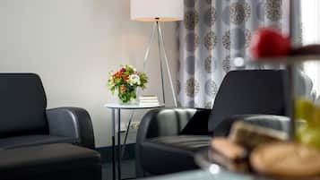 Ett hotellrum med två svarta läderfåtöljer, ett litet bord med en vas med blommor, en golvlampa och en gardin med ett blommönster.