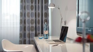 A modern hotel room with a white desk, a laptop, a bottle of water, and a glass. - Dorint Kongresshotel Düsseldorf/Neuss (Neuss)