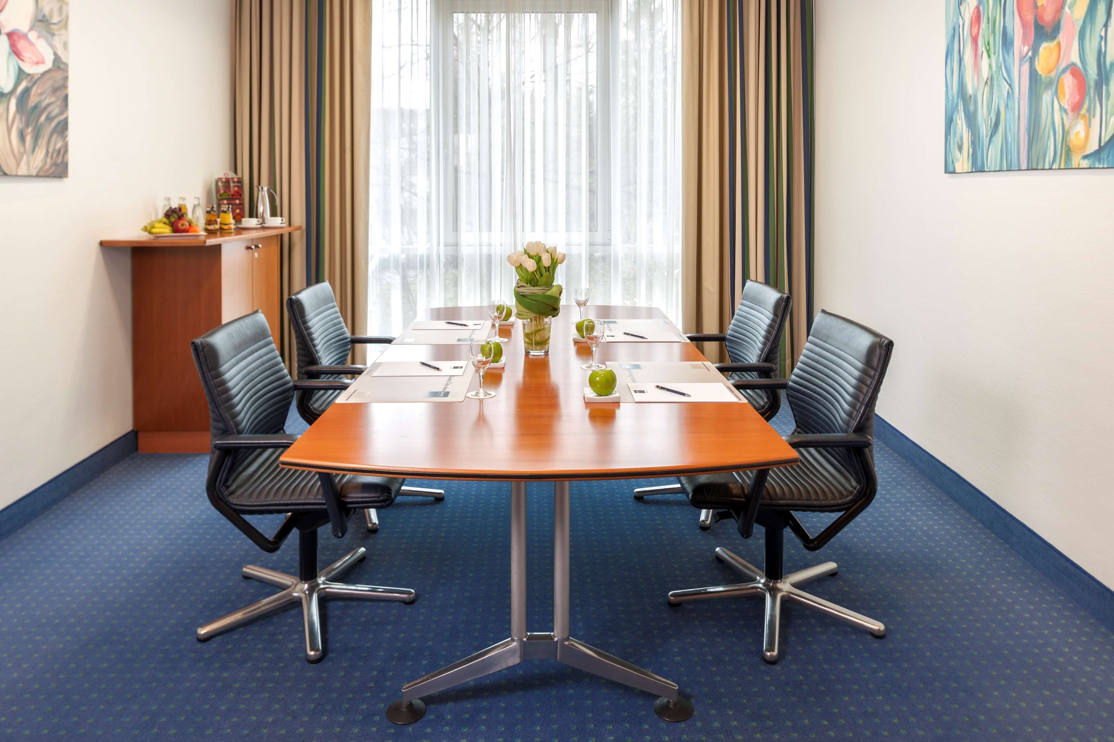 A conference room with a wooden table, four black chairs, a vase with flowers, and a small cabinet with items on it.