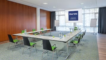 Una sala conferenze con un lungo tavolo, sedie verdi e uno schermo di proiezione che mostra 'Dorint'.