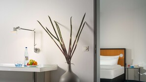 A hotel room with a bed, bedside table, lamp, vase with plants, and a fruit bowl. - Dorint Kongresshotel Düsseldorf/Neuss (Neuss)