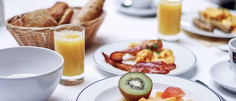 Una mesa de desayuno con diversos platos, como tostadas, huevos, tocino y fruta.