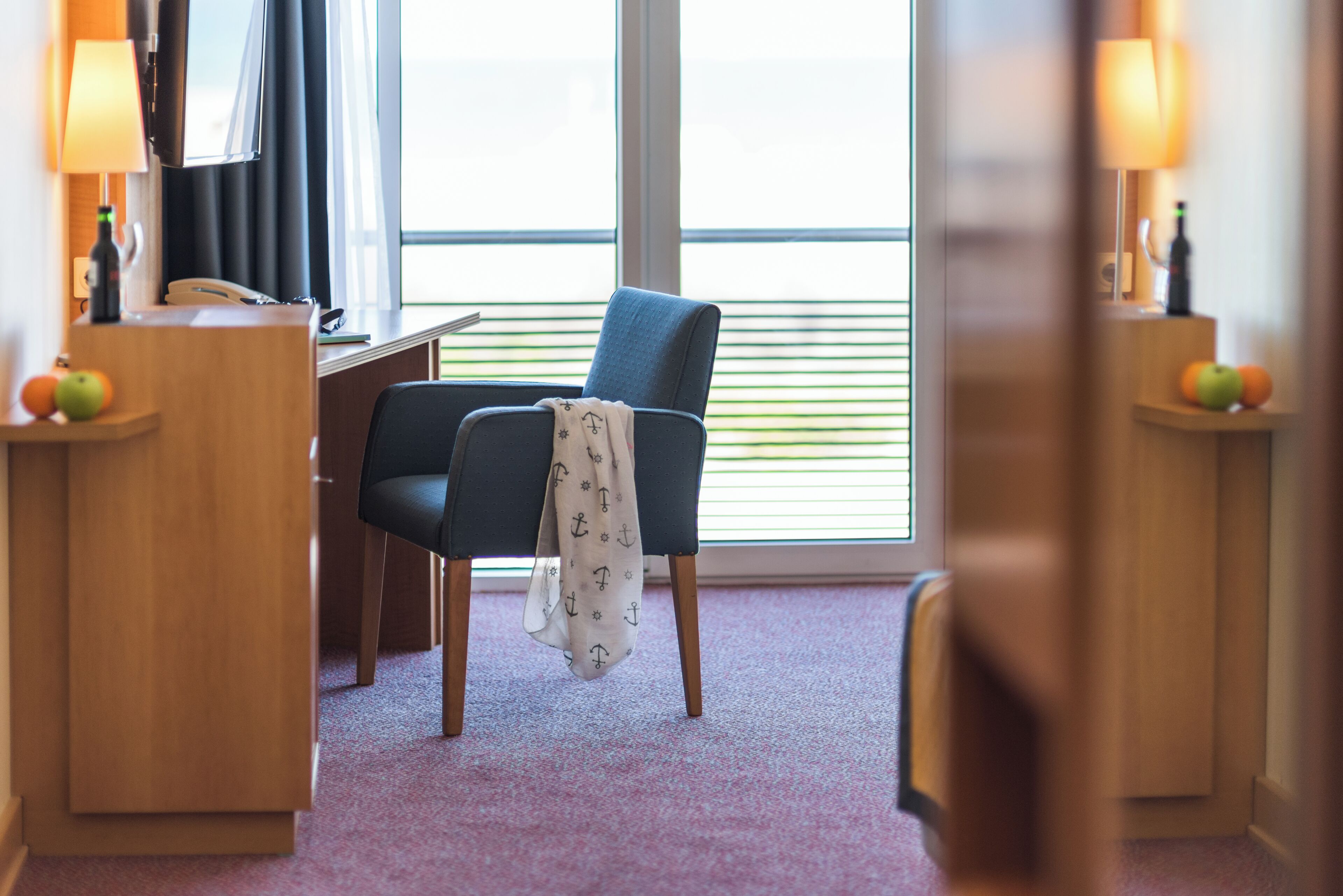 A hotel room with a desk, a chair, a lamp, and a window with blinds.
