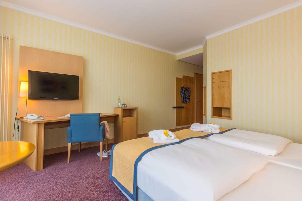 A hotel room with a bed, a desk, a chair, a television, and a wardrobe.