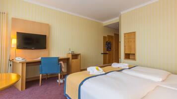 Una habitación de hotel con una cama, un escritorio, una silla, un televisor y un armario.